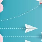 Paper airplanes flying in the sky with clouds and a red kite.