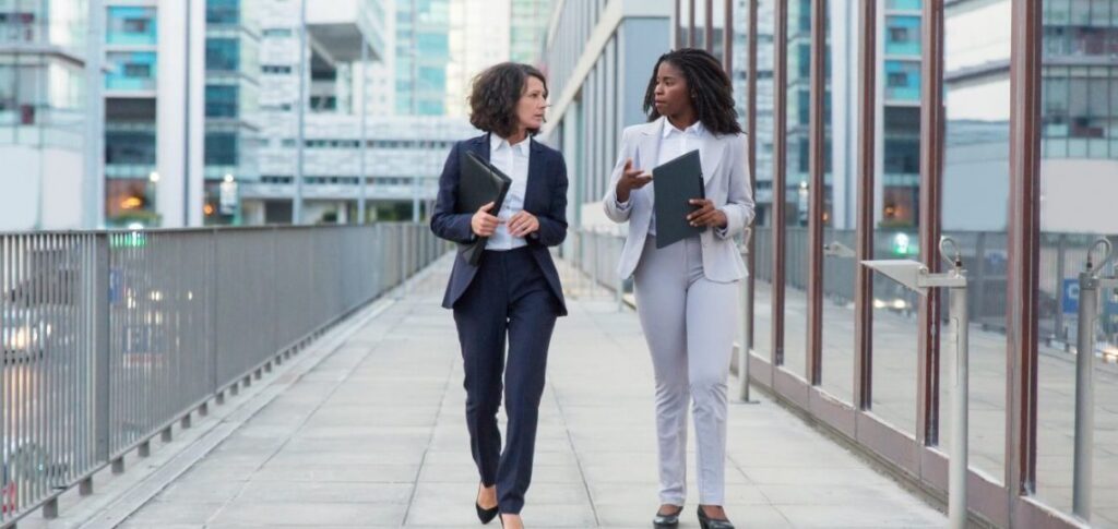 five-surprising-ways-to-reduce-stress-ebccoaching Two professional women walking and talking outdoors in business attire.