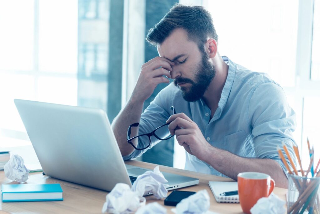 fm=f_3459 Stressed man working at his laptop, holding glasses and rubbing his forehead.