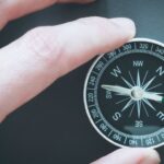 Hand holding a black and white compass showing directions.