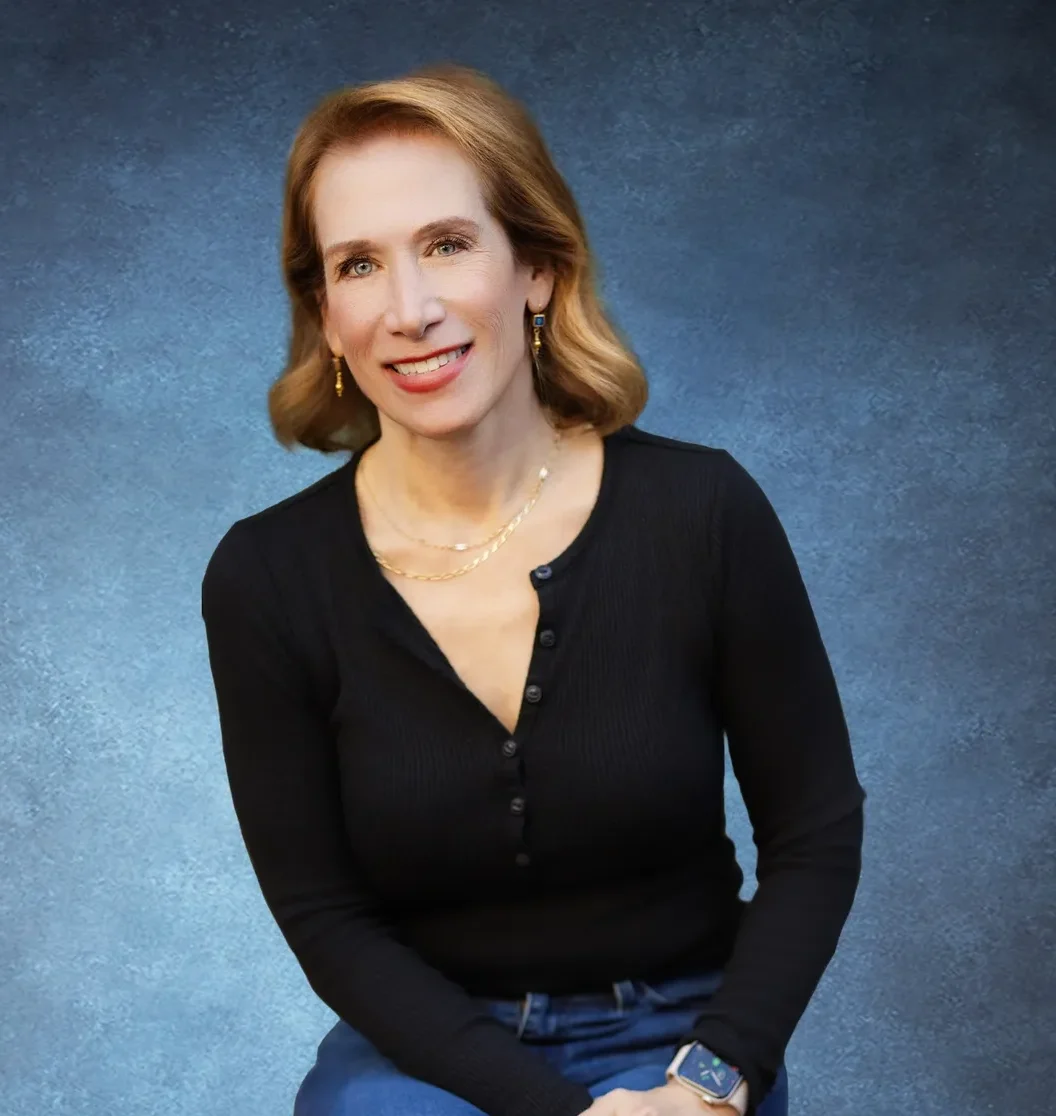 Woman with red hair wearing a black top poses against a blue background.