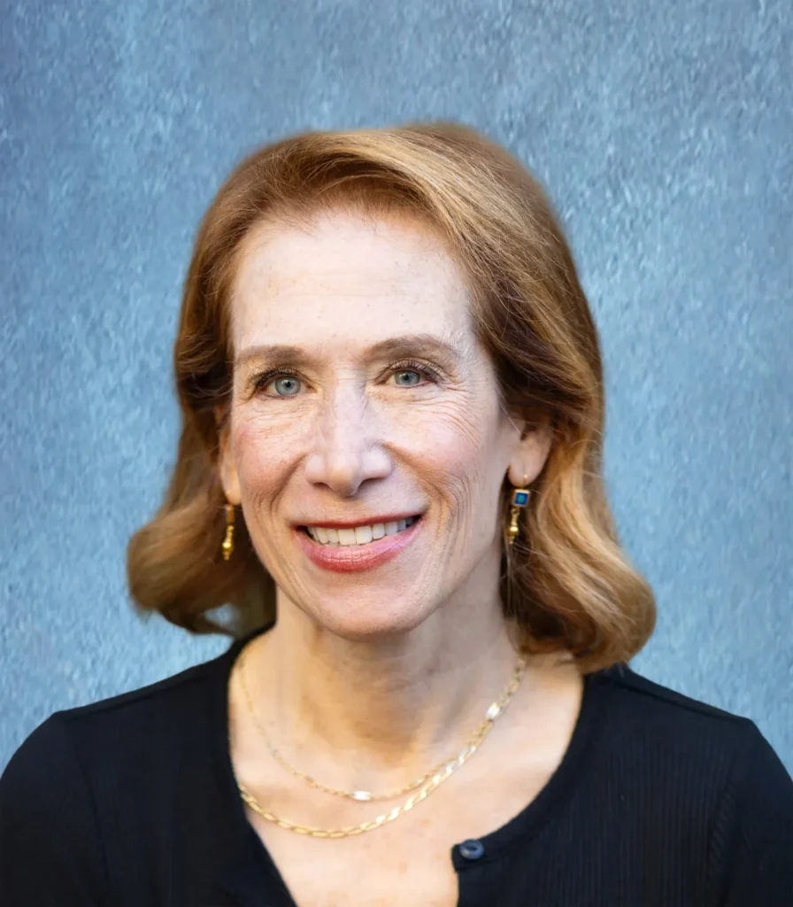 Portrait of a smiling middle-aged woman with light brown hair against a blue-gray background.
