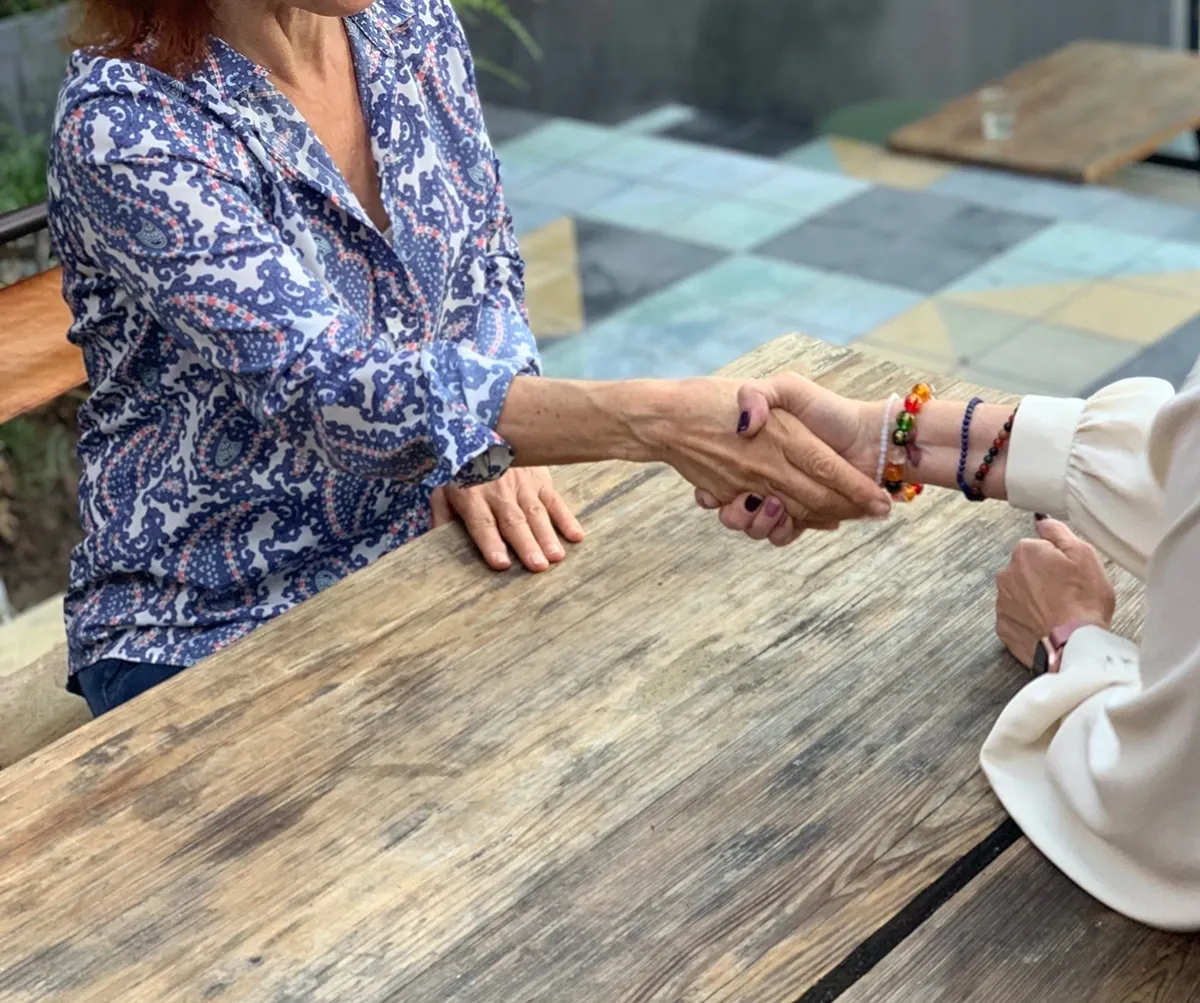 Two people shaking hands over a wooden table.